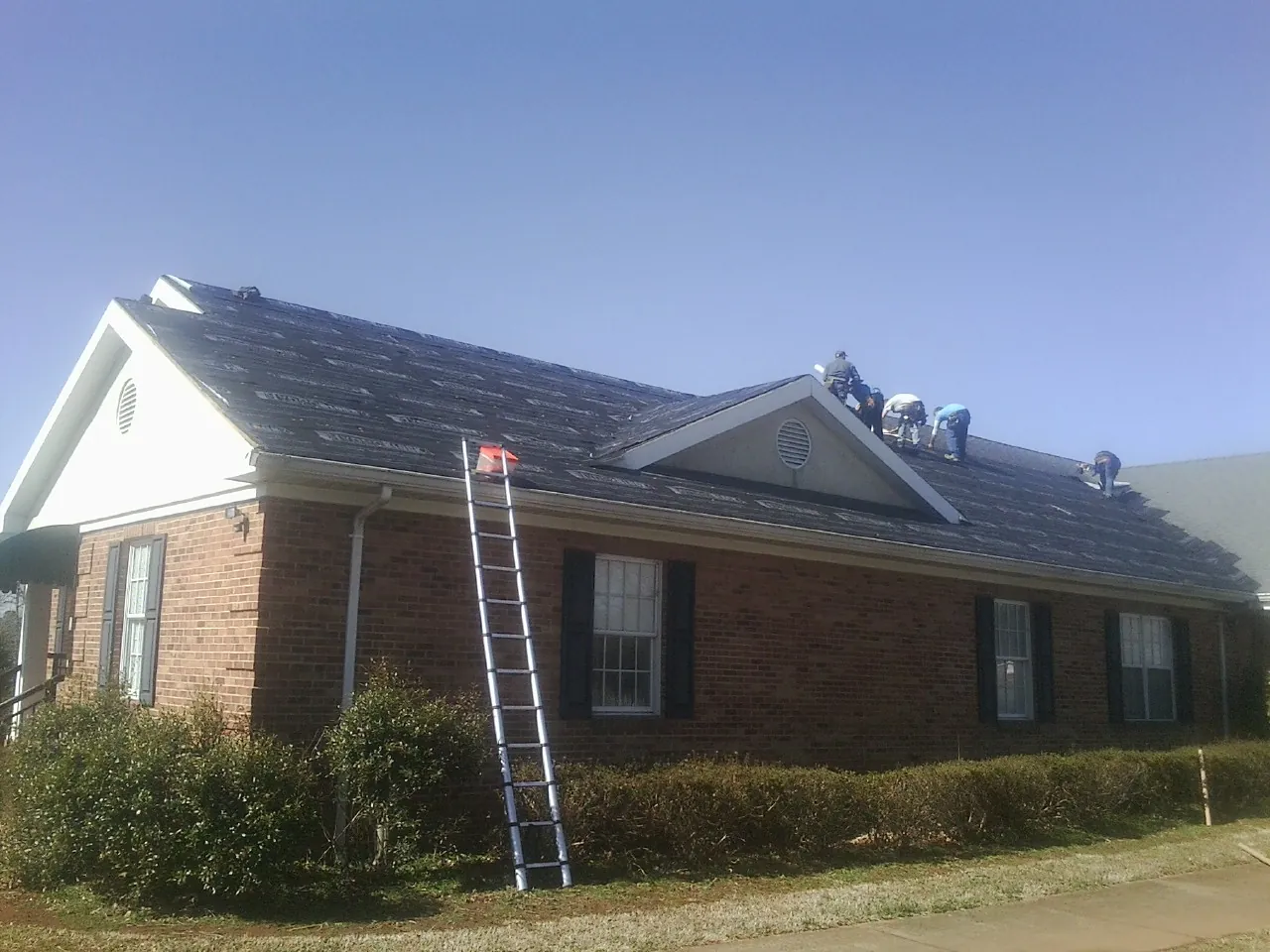 Crew tearing shingles off a brick ranch roof with a ladder set — Metal Roof Repair work by our crew in Cornersville