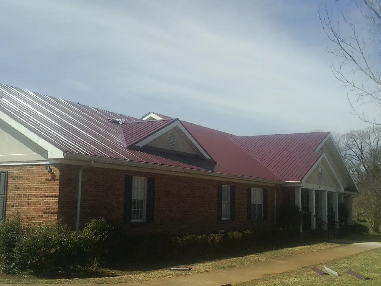 Red metal roof with gabled entries on a long brick building, from a Hail Damage Roof Repair job in Cornersville
