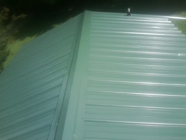 New green metal panels meeting at the ridge of a roof — Flat Roof Repair work by our crew in Cornersville