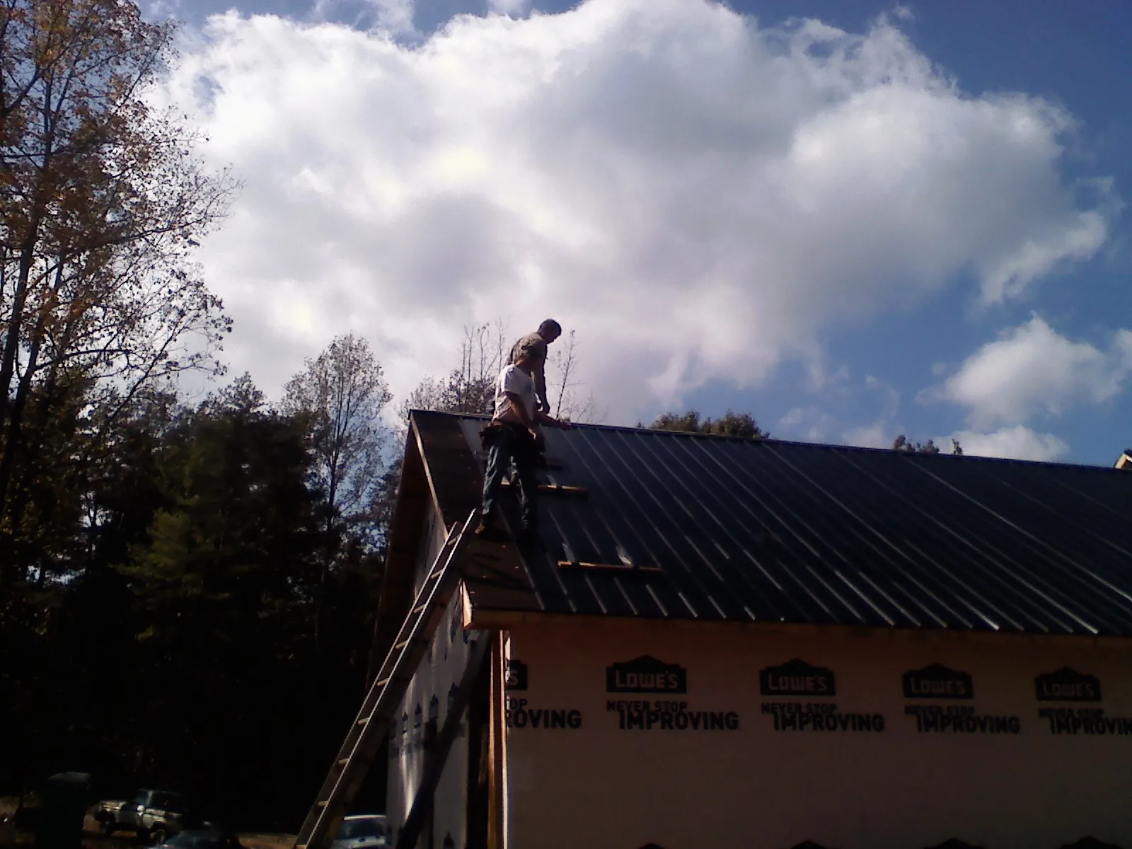 Roofer fastening dark metal panels high against a cloudy sky, from a Roof Inspection job in Cornersville
