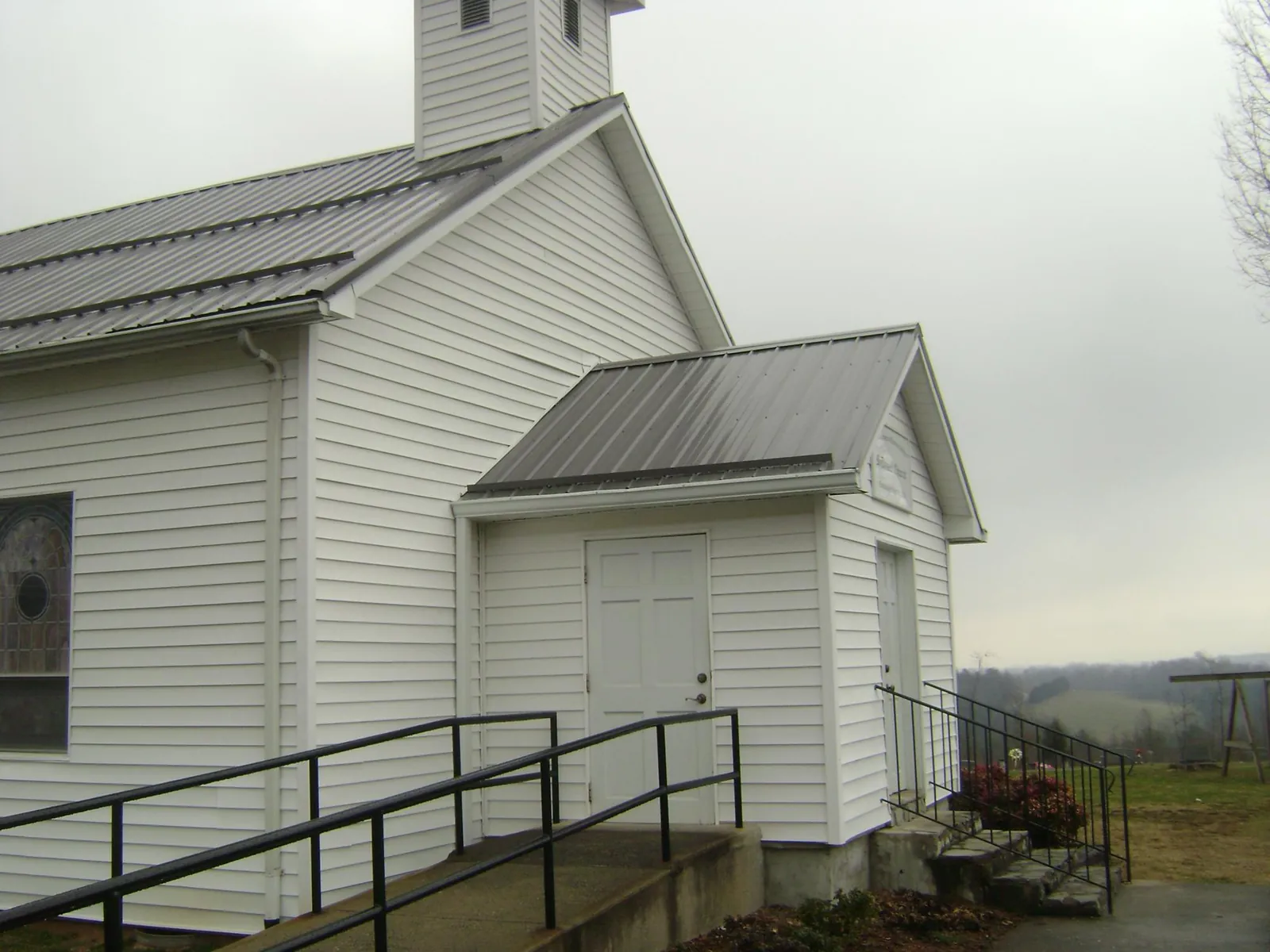 Gray metal roof on a white clapboard church with a steeple in Cornersville