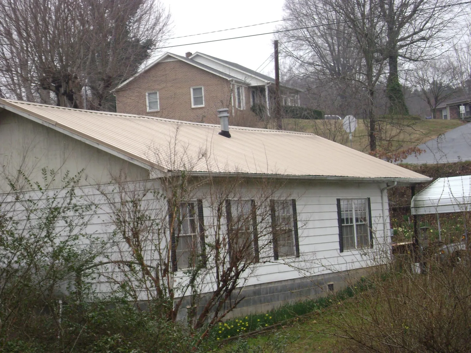 Tan metal roof on a white sided house set into a hillside — Commercial Roofing by Roofing Brothers in Cornersville