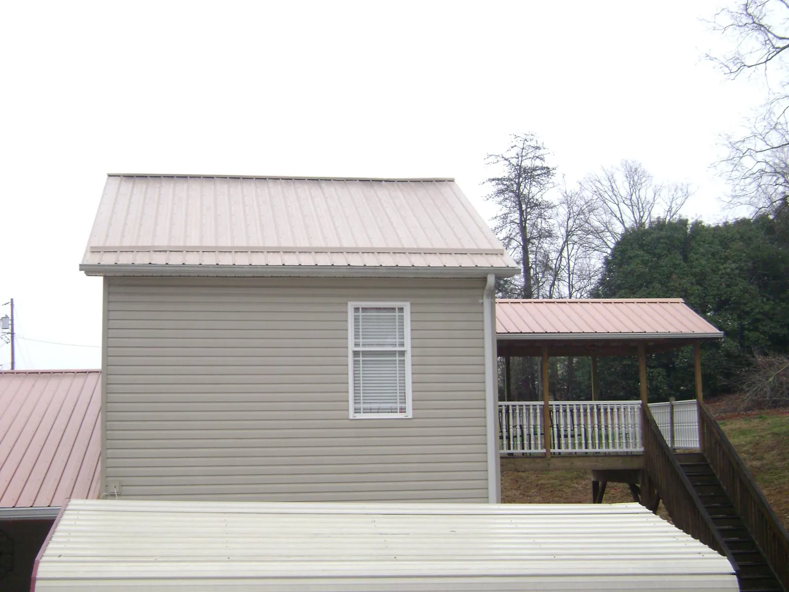 Tan metal roofs on a two story addition and attached porch, from a Roof Replacement job in Cornersville